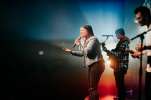 woman in white long sleeve shirt and red pants singing on stage — Foto por Chris na Unsplash